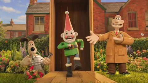 A promotional image of Aardman animated characters Wallace and Gromit standing in a garden next to an open shipping crate. A garden gnome is stepping out of the shipping crate.