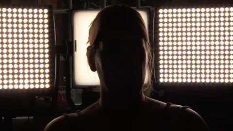 A silhouette of a woman, with bright lights behind her. She is not identifiable.