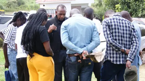 Peter Njoroge / BBC A group of relatives stand in a circle in prayer.