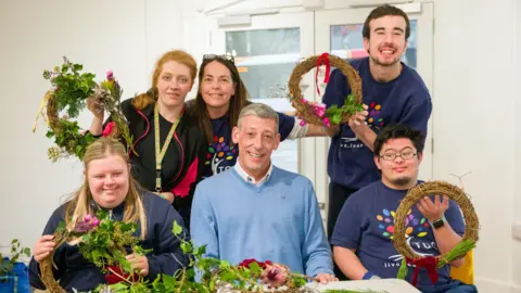 National Lottery Steve Thomson (centre) surrounded by young people making Christmas wreaths all posing indoors for a photo.