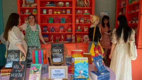 BBC Young women stand in a bookshop with various books on sale in the forefront 