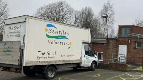 A white van is in a car park outside a brick building, with a space for wheelchair users next to it. The side of the van is emblazoned with "Bentilee Volunteers" and The Shed, which provides resale of furniture. A phone number is next to that.