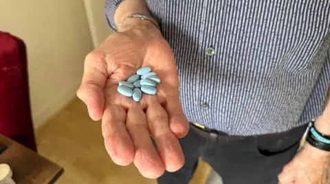 George King/BBC An open hand with blue tablets on its palm.
