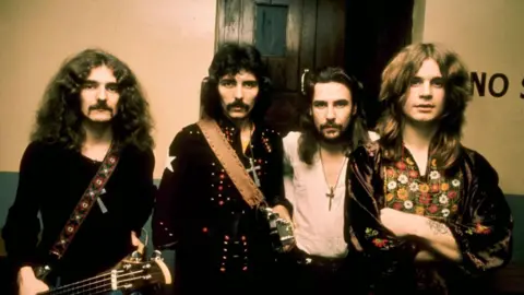 Getty Images A yellowing photo of four men with long hair in dark tops with two of them holding guitars