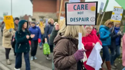 People marching outside the Ada Belfield care home in Belper. There's a sign that reads "care not despair"