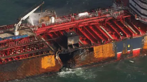 Close-up of the side of Stena Immaculate showing a large hole in its hull and signs of fire damage to the deck.