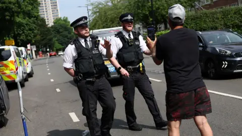 Two police officers talk to a protester, who has his back to the camera, on a road in London