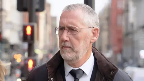 BBC Ian Harvey arriving outside the venue, wearing glasses, coat and tie