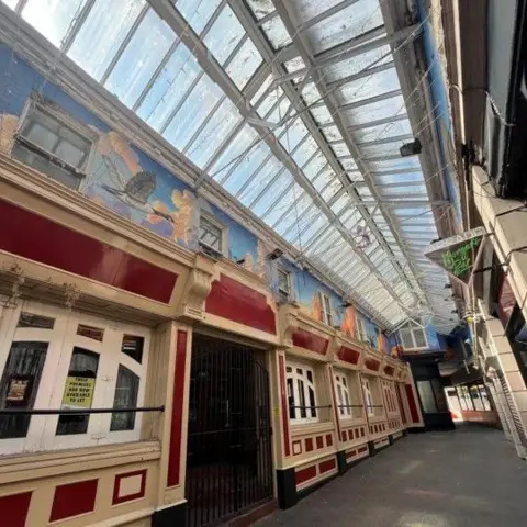 Cumberland Council The mural showing the brightly painted clouds and geese stretches out around Lowther Arcade. It has been painted underneath the roof windows and above the red shopfronts.