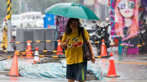 EPA A woman holding an umbrella walks in heavy rain, after multiple local governments across the island suspended work and classes to brace for Typhoon Gaemi; in New Taipei, Taiwan, 24 July 2024