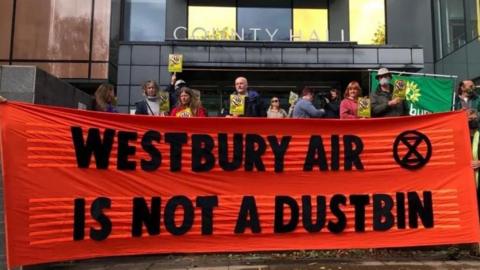 Protest outside Wiltshire Council, with people holding a big red banner saying 'Westbury air is not a dustbin'
