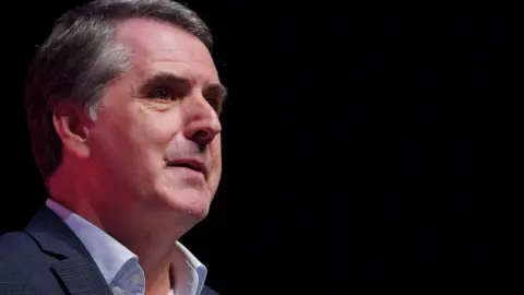 PA Media Side profile of Metro Mayor Steve Rotheram with grey hair wearing pale blue shirt and navy jacket. 