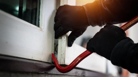 Burglar breaking into a window with a crowbar