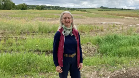 Kate Moser Andon/BBC Miranda Fyfe standing on a field with the Magog Down in the background