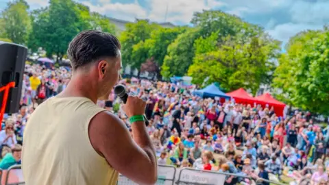 Pride in Gloucestershire A male singer performing on stage in front of a large crowd at Pride in Gloucestershire 2025