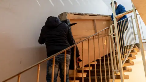 Getty Images Two people moving a sofa up a flight of stairs