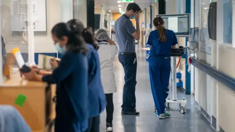 PA Media Doctors and nurses walking and standing in a busy hospital corridor.