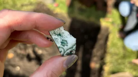 Supplied A view of someone holding a tiny shard of white pottery with a flower design.