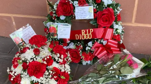 Marc Gaier/BBC Floral wreaths in red and white - a ribbon reads RIP Diogo