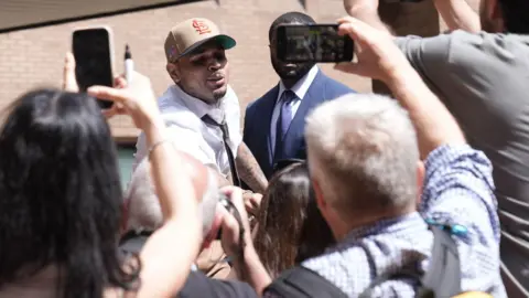 PA Media Chris Brown leaning into a small crowd outside court, with some holding up their phones