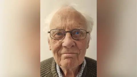 John Burdon has glasses and short white hair.