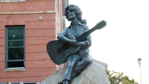 A statue of Dolly Parton sitting on a rock holding a guitar.