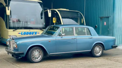 Steve Huntley/BBC The blue Rolls Royce is parked in a car park in front of two larger buses.