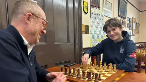 Frederick and Craig sitting at a table simulating a chess move.