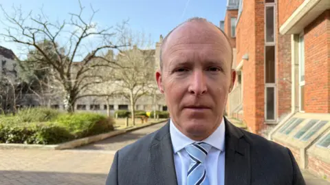 Ch Supt Roy Linden standing in front of the court building wearing a shirt and tie