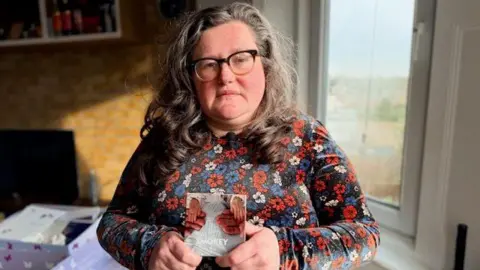 Alice Topping is wearing a floral dress and holding a picture of her daughter's hands that was taken in 2023