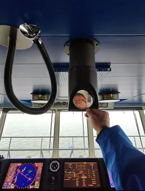 YouTube A man wearing glasses looks into a small mirror on a piece of equipment in the bridge of a large ferry 