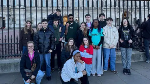 The Way Youth Zone A group of teenagers stand togther near some black fences outside Buckingham Palace in London