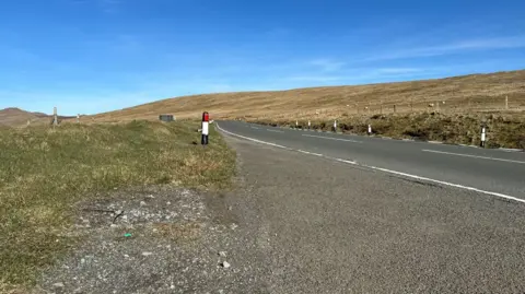 The Mountain Road looking in the northern direction. There is heathland on either side of the carriageway and a clear deep blue sky above.