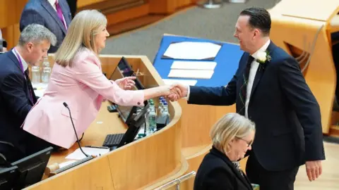 PA Media A man and woman in business wear shake hands 