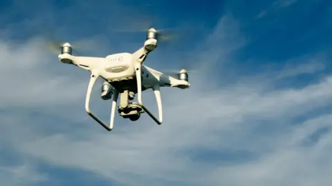 A white drone flying against a blue sky