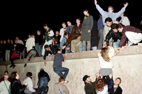 Reuters East German citizens climb the Berlin wall at the Brandenburg gate after the opening of the East German border was announced in Berlin on 9 November 1989