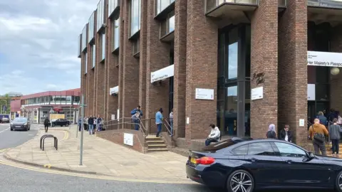 Jozef Hall/BBC People outside passport office in Peterborough