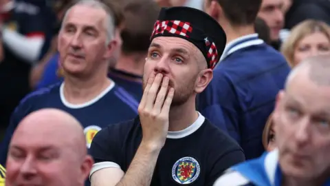 Getty Images a worried Scotland football fan, wearing a Scotland strip and tartan hat, holds his hand to his mouth