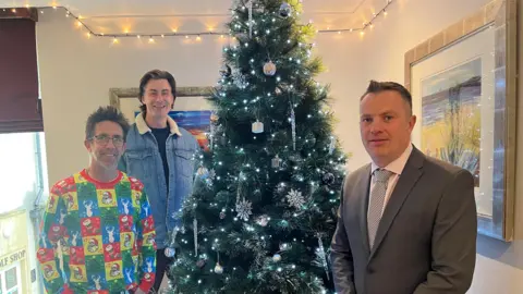 Three men stand beside a decorated Christmas tree