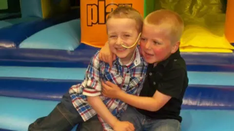 Ryan Quinn two small blond-haired boys hug in a soft play area