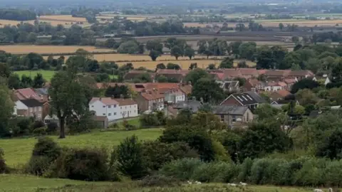 BBC A birdseye view of Bishop Wilton from above. In between hills and greenery, several large buildings can be seen.