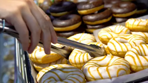 Getty Images Person picking up doughnuts in a supermarket