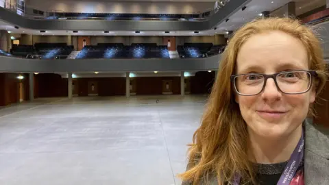 AEG Crissie Rushton with red hair and glasses standing in an empty Wolverhampton entertainment venue