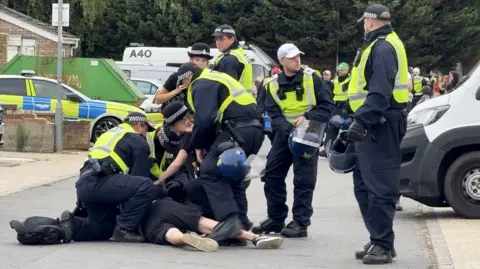 A group of police around a man being arrested on the ground.