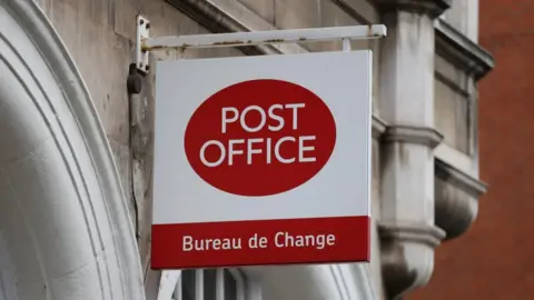 Reuters A stock image shows a 'Post Office' sign on the exterior wall of a branch