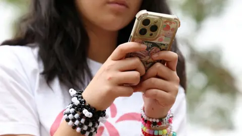 Close up image of an anonymous young girl wearing a white T shirt and colourful bead bracelets while using her smartphone outdoors, taken in Sydney in November.