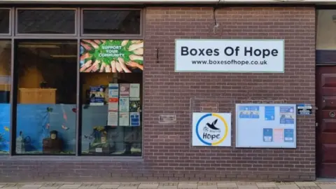 Boxes of Hope The Boxes of Hope hub in Holbeach with signs on the wall on the wall and posters in the window. One of the images depicts a dove holding an olive branch and has the word 'Hope' written underneath.