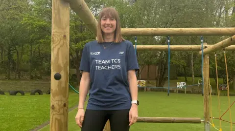 Kelly Rowland The image shows a woman standing on a climbing frame, wearing a dark blue shirt that says "Team TCS Teachers" in white text.