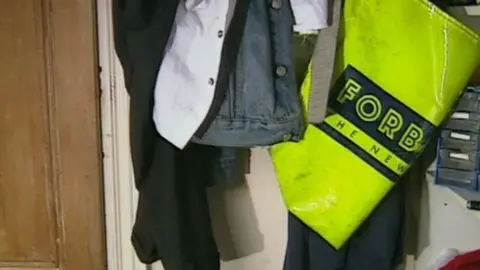 A picture showing a yellow bag for delivering newspapers hung up on a wall next to a denim jacket 