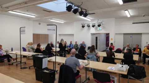 Tim Baldwin/KLBC People sit at tables in a hall, counting pieces of paper for the by-election